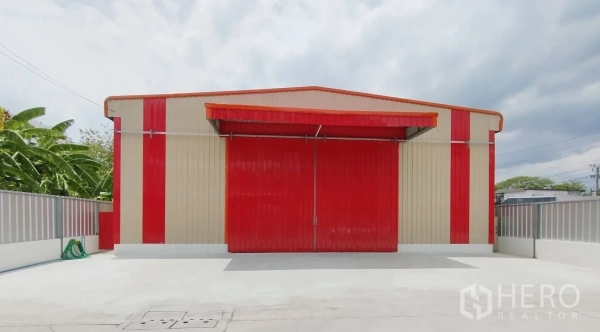 Warehouse for rent in Bang Khen, Bangkok - Close-up facade of the warehouse with red doors closed, beige and red cladding, and fenced perimeter.