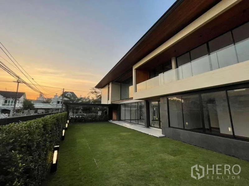 Detached House for rent in Bang Phli, Samut Prakan - Contemporary rear facade with wide lawn and hedge fence at sunset