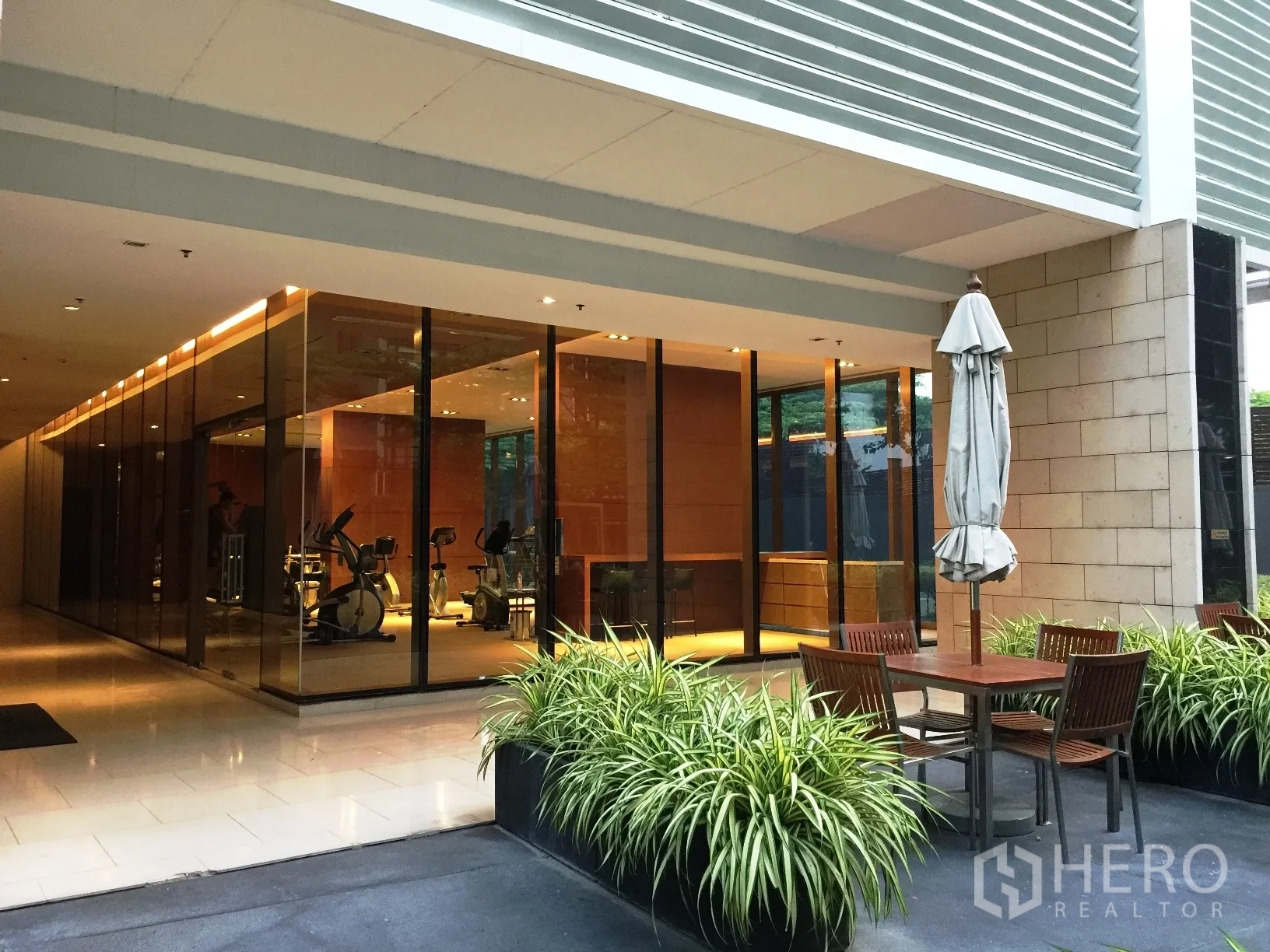 Condominium for rent or sale in Khlong Toei, Bangkok - Glass-walled fitness centre with cardio machines and outdoor seating area.