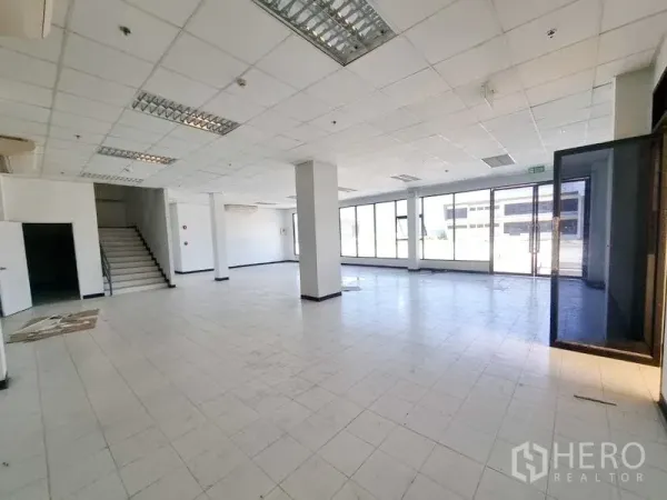 Factory for rent in Bang Pakong, Chachoengsao - Open-plan ground-floor office or showroom with staircase, full-height windows, and tiled floors.