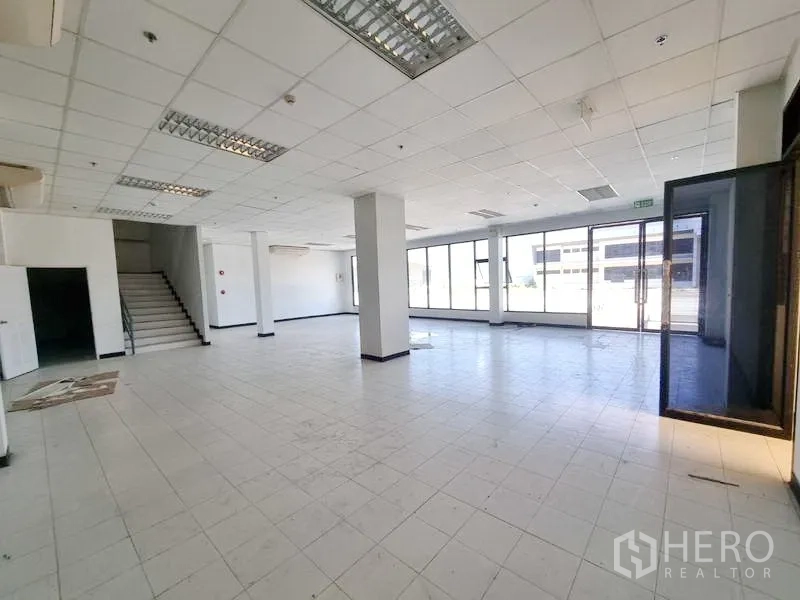 Factory for rent in Bang Pakong, Chachoengsao - Open-plan ground-floor office or showroom with staircase, full-height windows, and tiled floors.