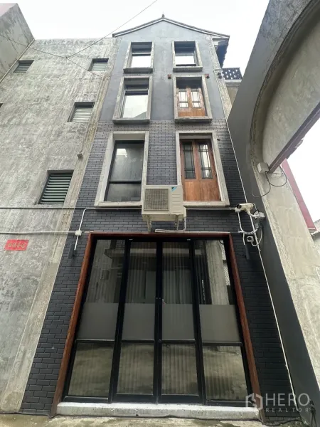 Home Office for rent in Pathum Wan, Bangkok - Rear grey-brick facade with tall windows and an AC unit above a black-framed entrance.