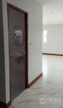 Warehouse for rent in Lam Luk Ka, Pathum Thani - Hallway with restroom entrance and sink beside a light-filled tiled office area.