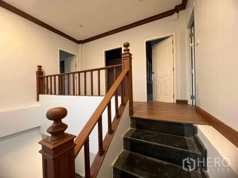 Detached House for sale in Bang Na, Bangkok - Stair landing with wooden balustrade and dark granite steps leading to bedrooms.