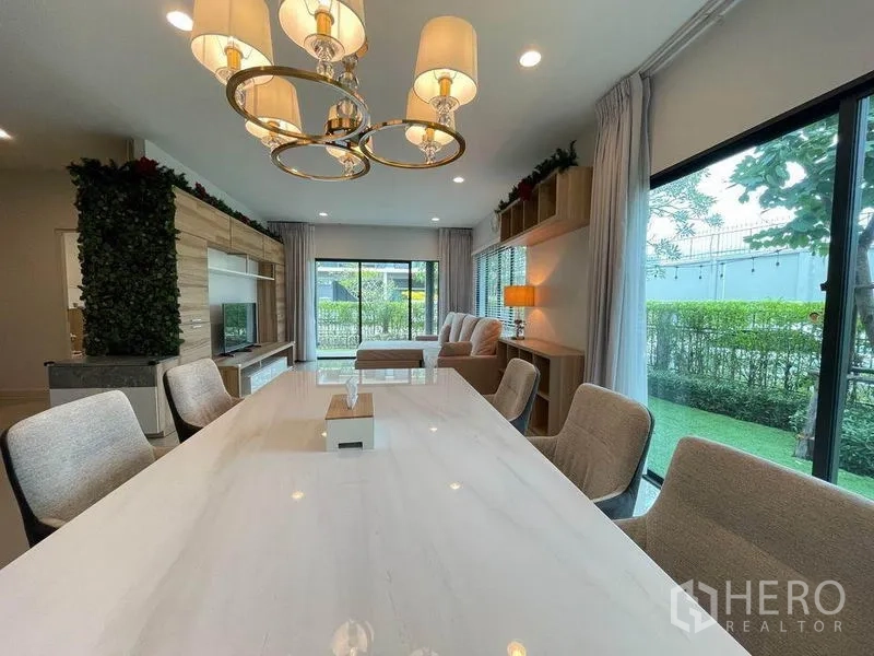 Detached House for sale in Pak Kret, Nonthaburi - Dining room with marble table, chandelier and floor-to-ceiling windows overlooking the garden.