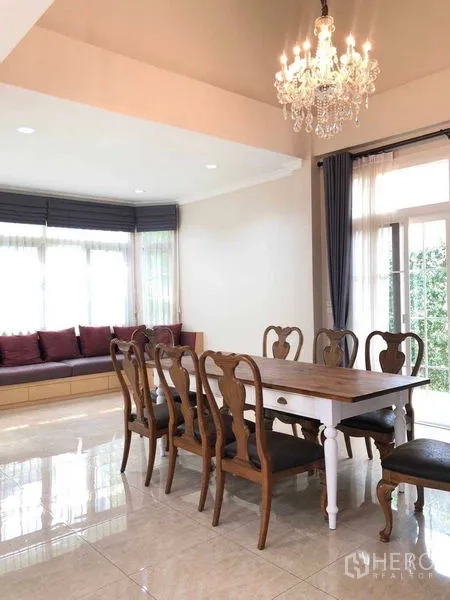 独立式住宅 出租在Bang Na, Bangkok - 明亮餐厅，长木桌、吊灯与靠窗坐榻，面向花园。