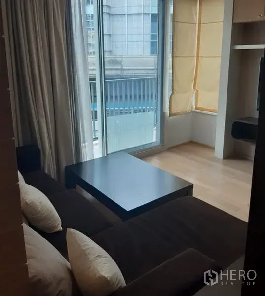 Condominium for rent in Khlong Toei, Bangkok - Living room with floor-to-ceiling windows, coffee table and sliding door to balcony.