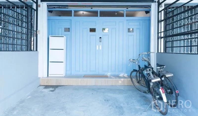 Townhouse for rent in Khlong Toei, Bangkok - Covered carport with pastel blue security door and two bicycles at the townhouse entrance.