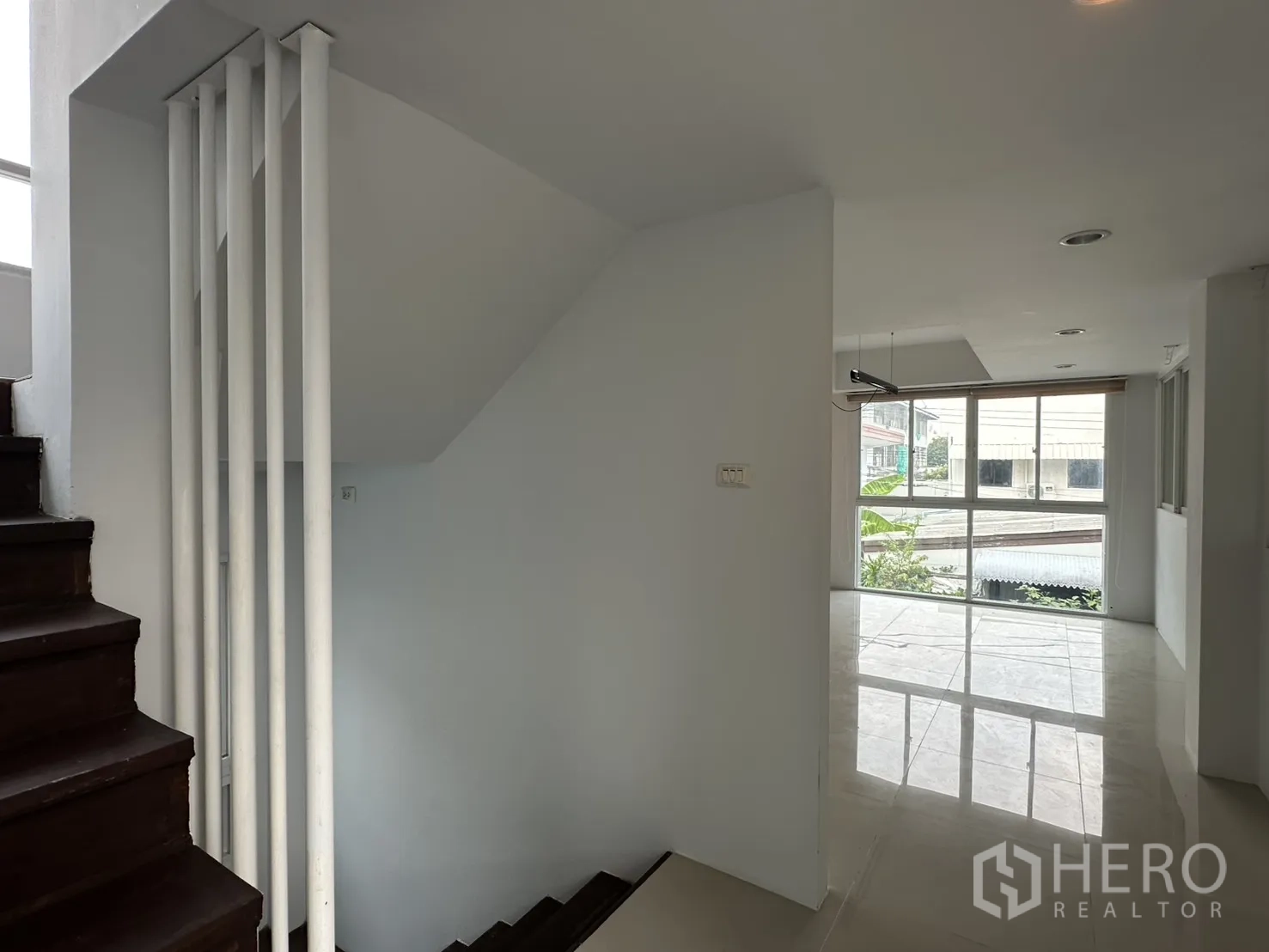 Home Office for rent in Watthana, Bangkok - Stair landing opening to a bright living area with large windows and glossy tile floor.