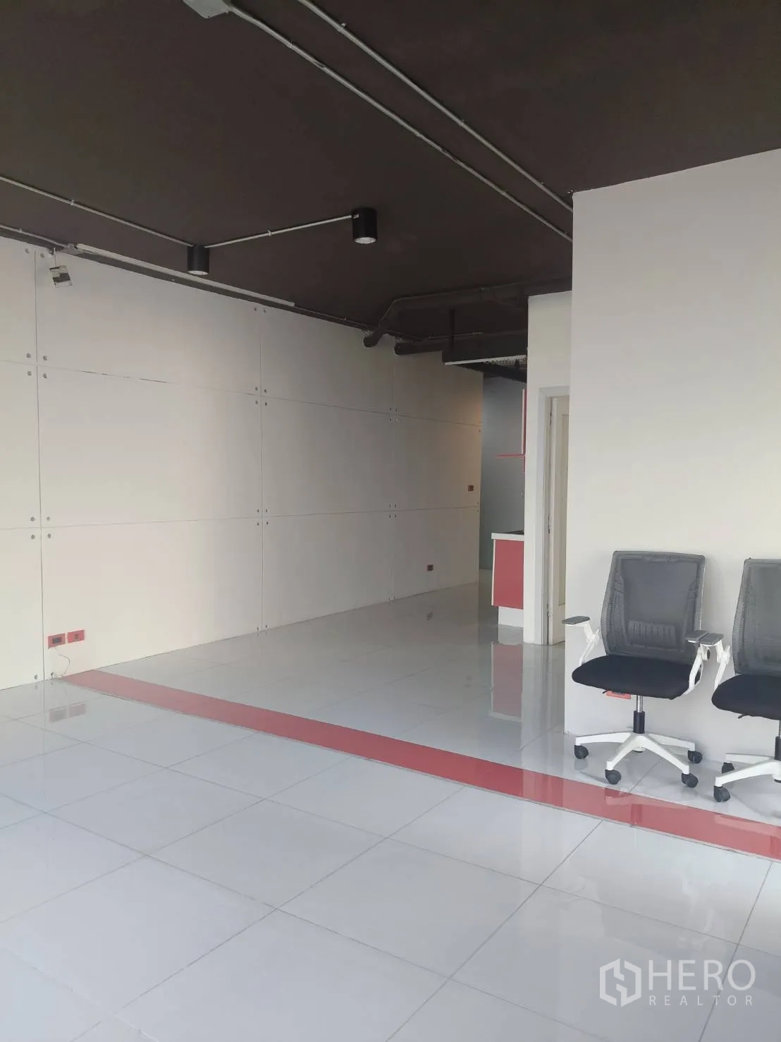 Office Space for rent in Khlong Toei, Bangkok - Open workspace with glossy white tiles, a red accent stripe and two office chairs.