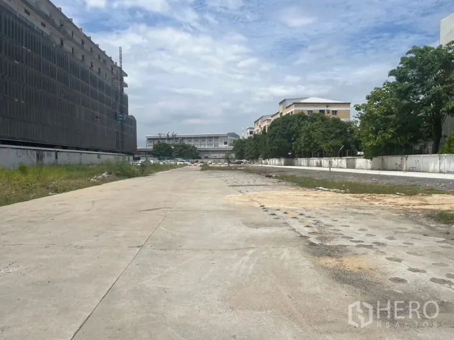 地 出租在Bang Khun Thian, Bangkok - 开阔混凝土地块，四周有围墙，夹在低层建筑与树木之间。
