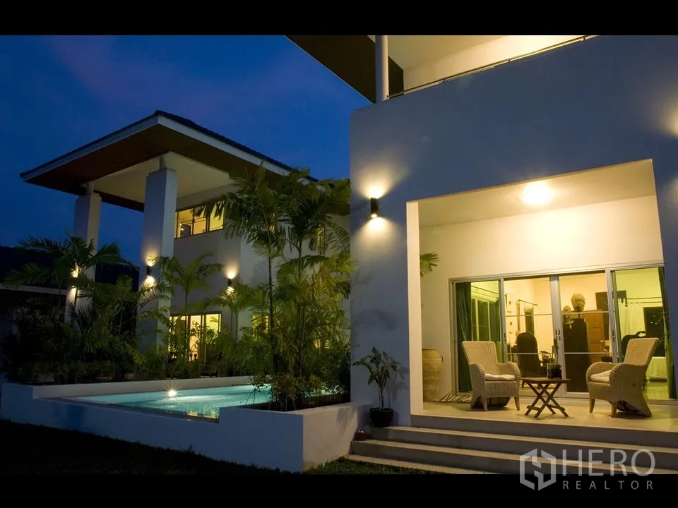 Detached House for rent in Khan Na Yao, Bangkok - Covered terrace with wicker seating beside the lit swimming pool and large sliding glass doors to the living room.