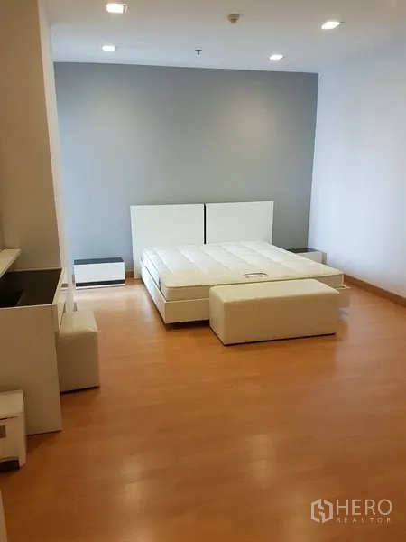 Condominium for rent in Khlong Toei, Bangkok - Spacious bedroom with platform bed, wood flooring, bedside tables, and a soft grey feature wall.