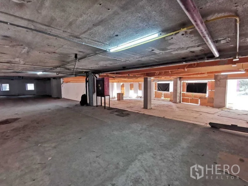 Retail Space for rent in Khlong Toei, Bangkok - Spacious shell retail interior with exposed ceiling, concrete floors, pillars, and fluorescent lighting.