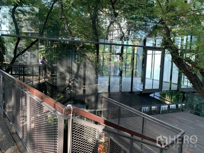 Office Space for rent in Khlong Toei, Bangkok - Elevated metal walkway and glass-walled pavilion nestled among mature trees.