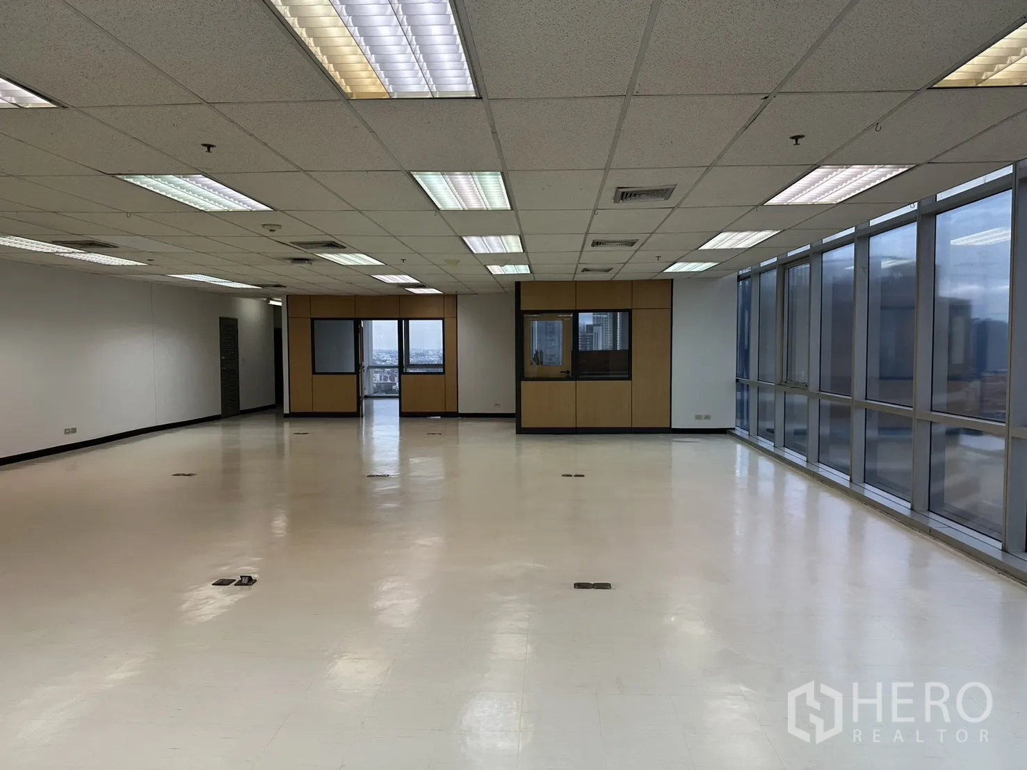 Office Space for rent - Bright office area with a wall of windows and two partitioned meeting rooms under fluorescent lighting.