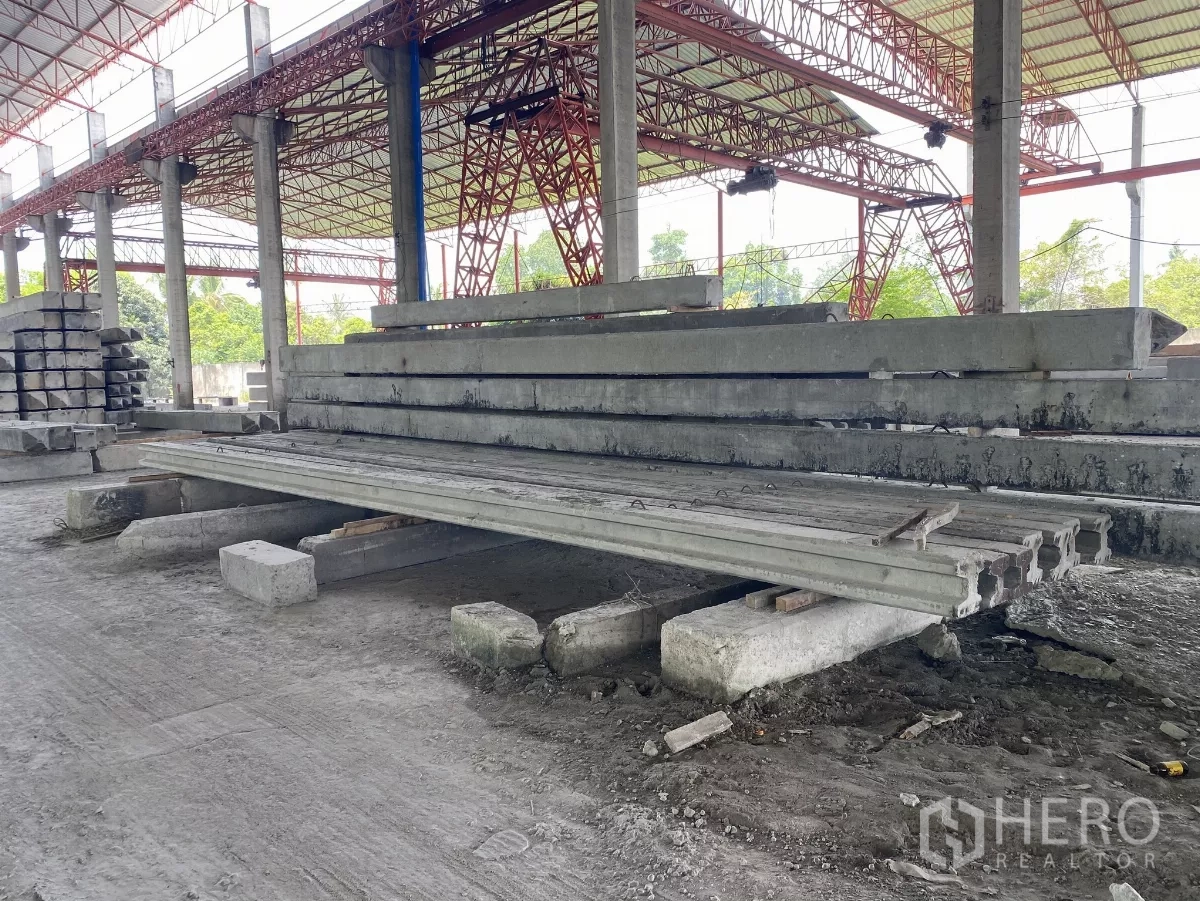 Factory for sale in Chon Buri - Stacks of precast concrete slabs and beams stored under the high steel roof.