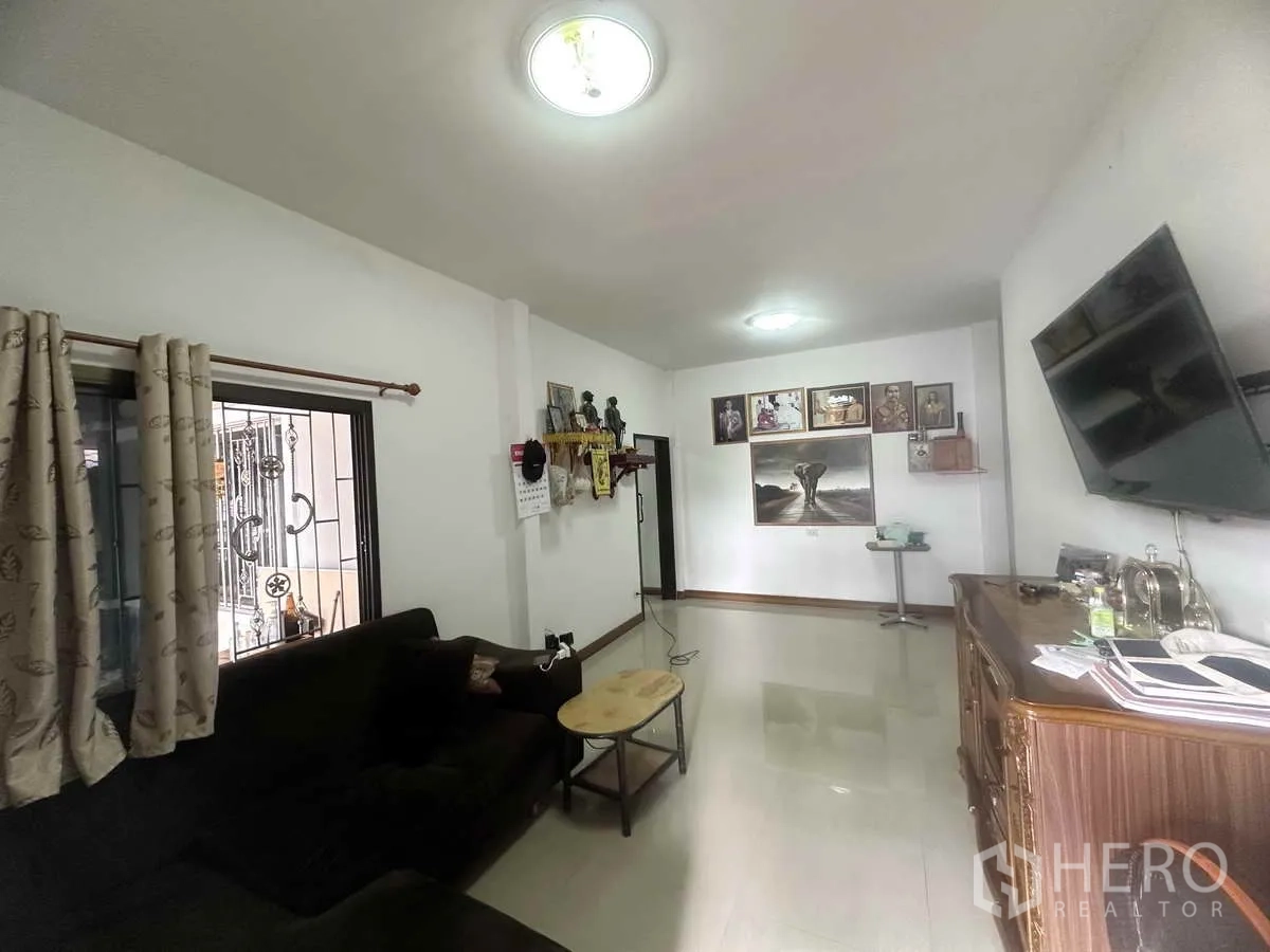 Detached House for sale in Pathum Thani - Living room from another angle with sofa, TV and wall art.