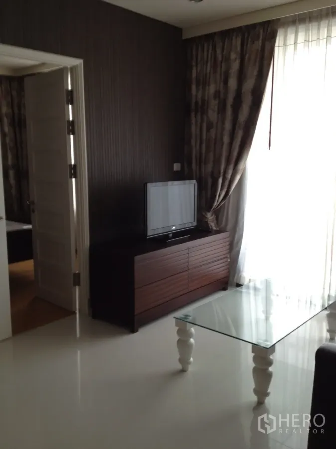 Condominium for rent in Khlong Toei, Bangkok - Modern living room with TV console, glass coffee table and sheer curtains.