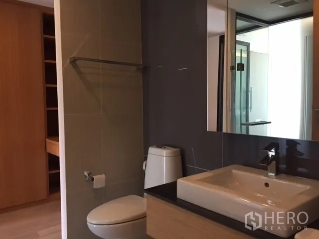 Condominium for rent or sale in Pathum Wan, Bangkok - Modern bathroom with large mirror, vanity countertop and toilet.