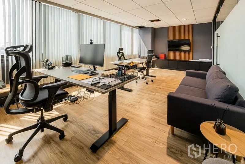 Office Space for rent - Executive office with sit-stand desks, sofa and media wall beside vertical blinds.