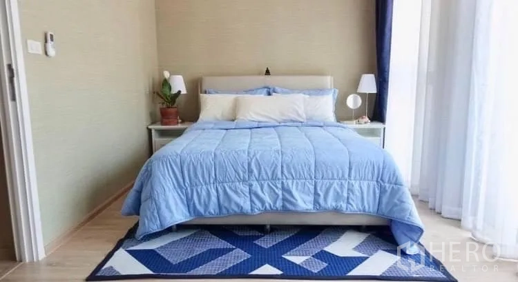 Townhouse for rent or sale in Suan Luang, Bangkok - Sunlit bedroom with blue bedding, bedside tables and sheer curtains.