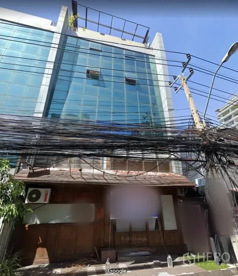 Retail Space for rent in Khlong Toei, Bangkok - Street-front retail unit with wooden facade beneath a mid-rise glass building in Thonglor, with visible power lines and a utility pole.