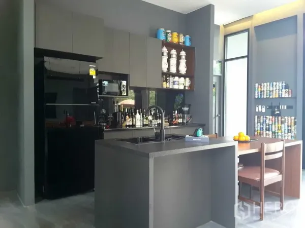 Detached House for rent or sale in Lam Luk Ka, Pathum Thani - Sleek dark-toned pantry kitchen with island sink, black appliances, open shelving and a small dining set.