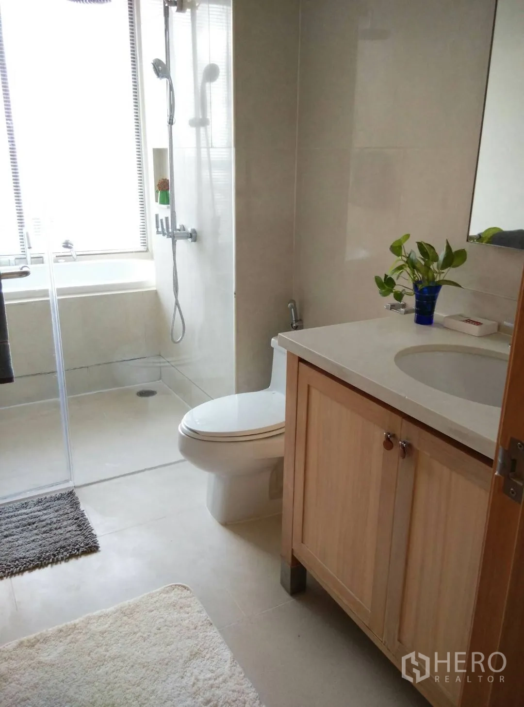 Condominium for rent or sale in Khlong Toei, Bangkok - Modern bathroom featuring a glass-enclosed shower, bathtub by the window, wooden vanity with sink and toilet.
