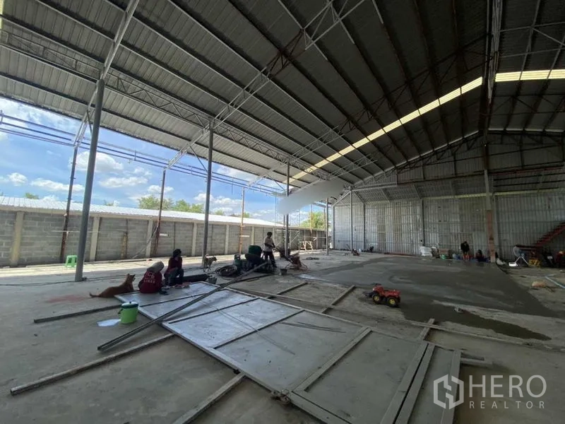 Warehouse for rent in Khlong Luang, Pathum Thani - Large covered work area with open sides, steel trusses and concrete flooring.