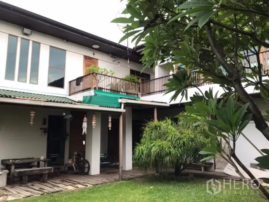 Detached House for sale in Lat Phrao, Bangkok - Rear exterior of two-storey house with balcony, covered terrace and landscaped lawn.