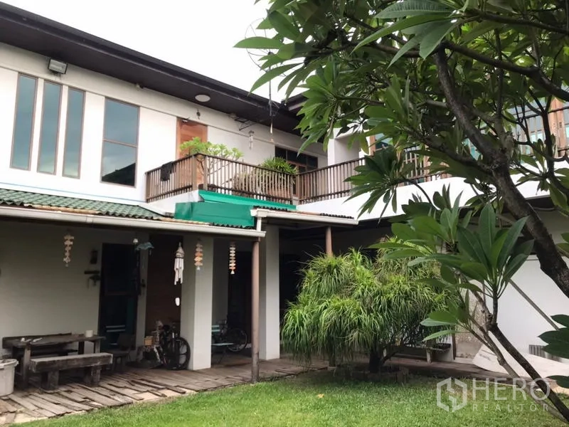 Detached House for sale in Lat Phrao, Bangkok - Rear exterior of two-storey house with balcony, covered terrace and landscaped lawn.