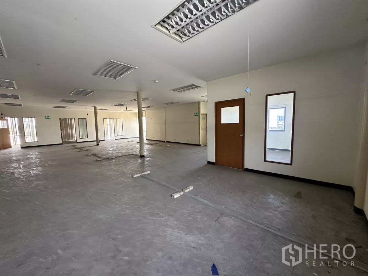 Warehouse for rent in Suan Luang, Bangkok - Open office area with a door to a private room and grid ceiling lights.