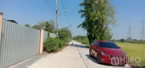 货栈 出租在Khlong Sam Wa, Bangkok - 通往仓库的安静道路，沿线电线杆与田野，路边停有汽车。