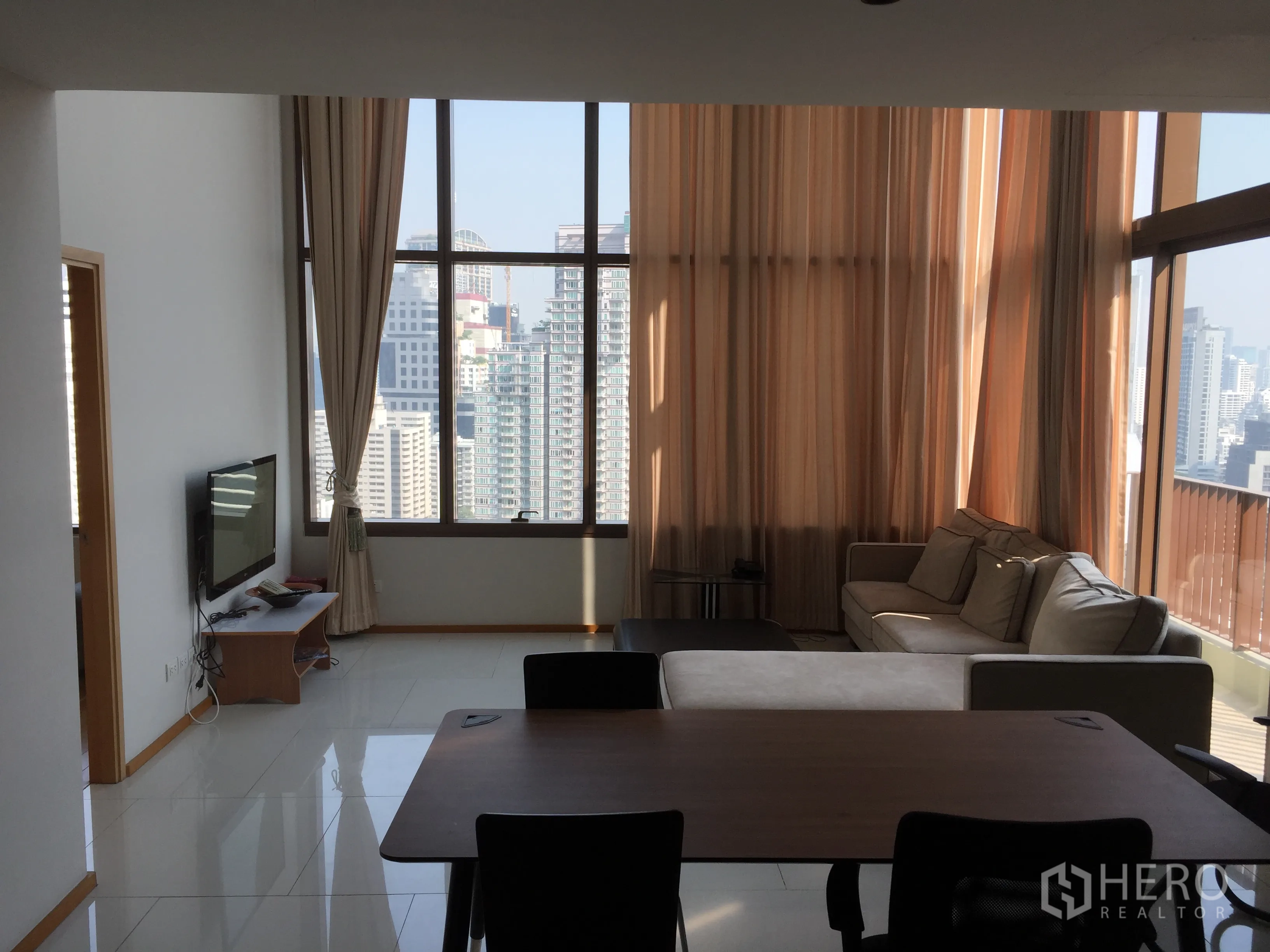 Condominium for rent or sale in Khlong Toei, Bangkok - Living room with floor-to-ceiling windows, city skyline view, sofa and dining table.