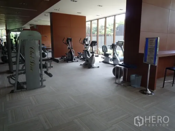Condominium for rent in Khlong Toei, Bangkok - On-site fitness center with cardio and weight machines beside large windows.