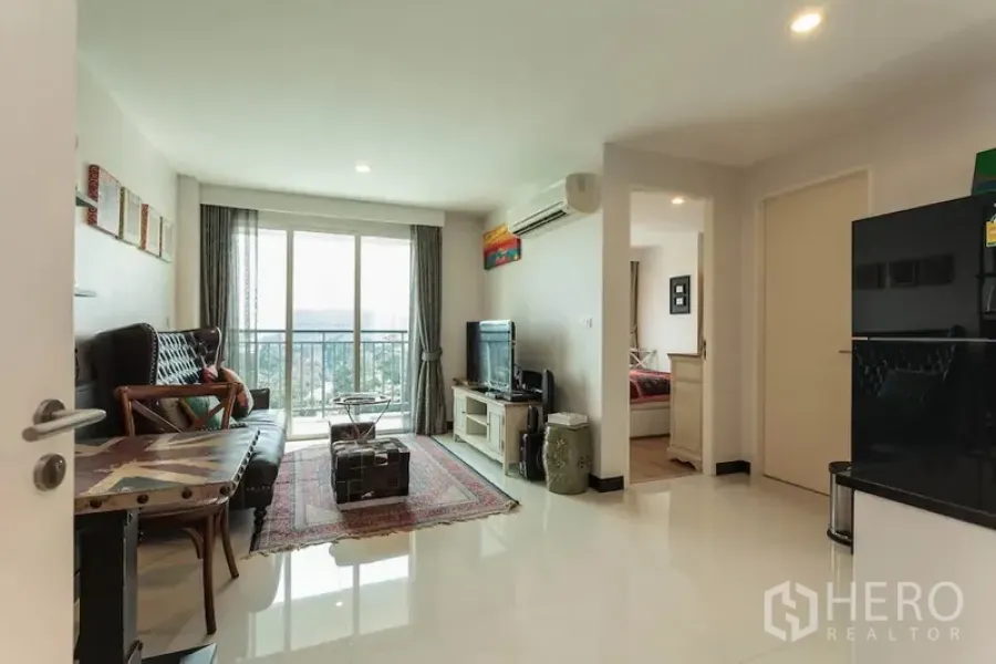 Condominium for rent in Khlong Toei, Bangkok - Bright living room with balcony and city view, TV unit, and doorway to the bedroom.