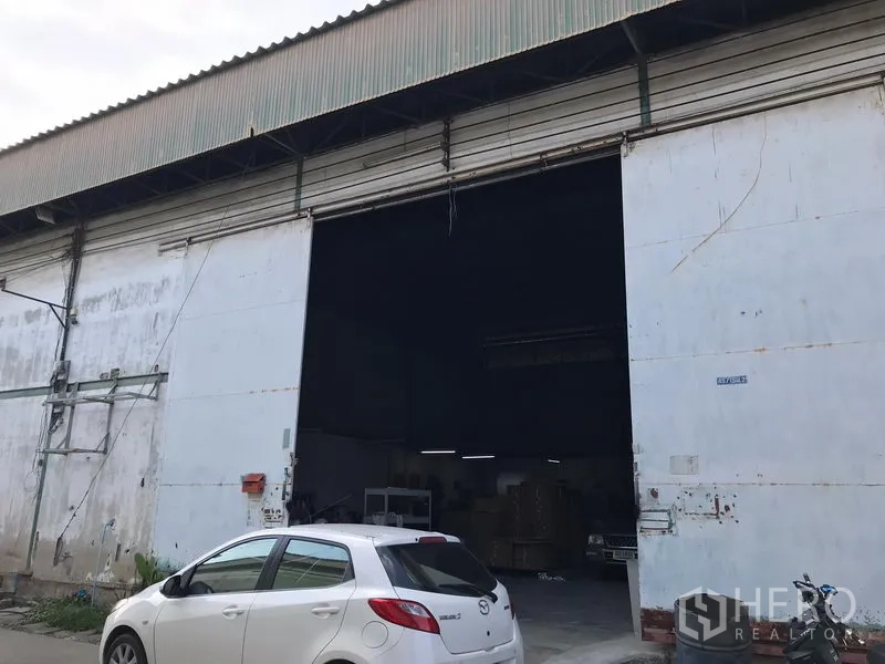 Warehouse for rent in Bang Phli, Samut Prakan - Industrial warehouse facade with extra-wide steel shutter door, high-clearance entrance and on-site parking area.