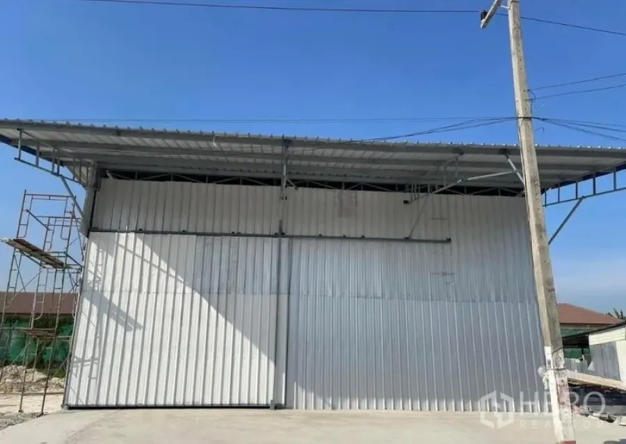 Warehouse for rent in Min Buri, Bangkok - Street-side view of corrugated metal warehouse facade with power pole and scaffolding.