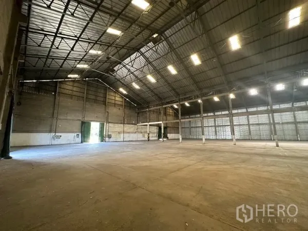 Warehouse for rent in Mueang Pathum Thani, Pathum Thani - Corner view of the warehouse showing bright ceiling lights, ventilation panels and wide entry door.