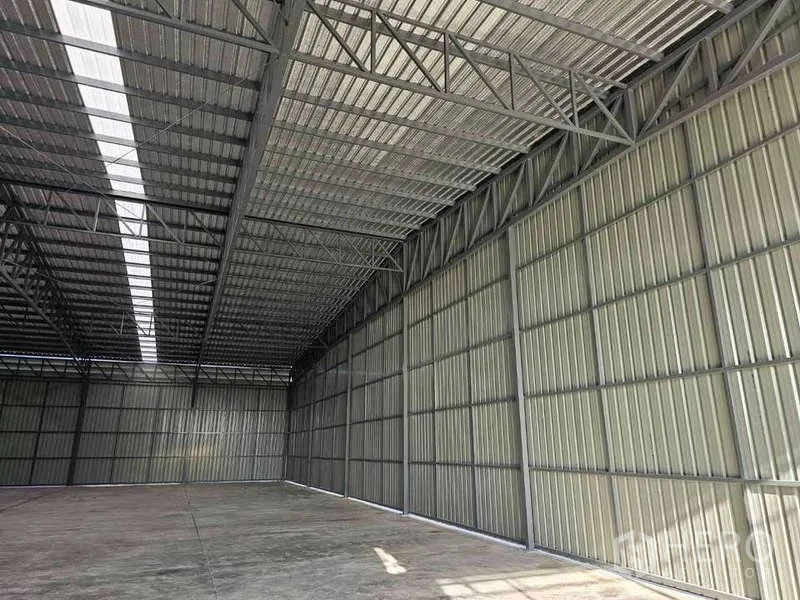 Warehouse for rent in Pak Kret, Nonthaburi - Side wall of warehouse interior with metal cladding and daylight panels over concrete floor.