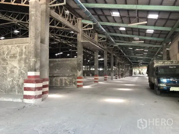 Warehouse for rent in Thanyaburi, Pathum Thani - Long warehouse aisle with truck parking, ventilation ducting and reinforced concrete pillars.