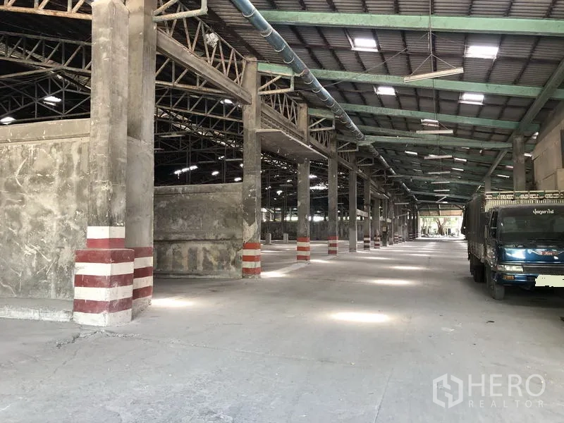 Warehouse for rent in Thanyaburi, Pathum Thani - Long warehouse aisle with truck parking, ventilation ducting and reinforced concrete pillars.