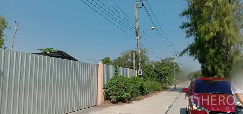 货栈 出租在Khlong Sam Wa, Bangkok - 靠近仓库的道路围墙与金属栅栏，沿街电力线路，路边停有车辆。