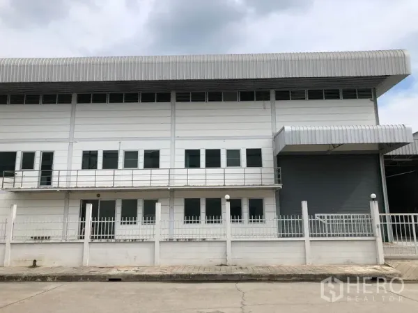 Factory for rent in Lam Luk Ka, Pathum Thani - Front facade of the industrial building showing balcony, rows of windows and a covered loading bay with shutter door.
