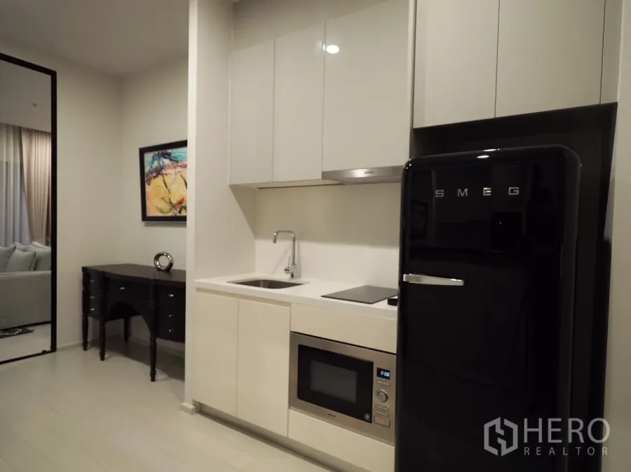 Condominium for rent or sale in Pathum Wan, Bangkok - Modern compact kitchen with glossy cabinets, sink, cooktop, microwave and a black SMEG refrigerator in a Bangkok condo.