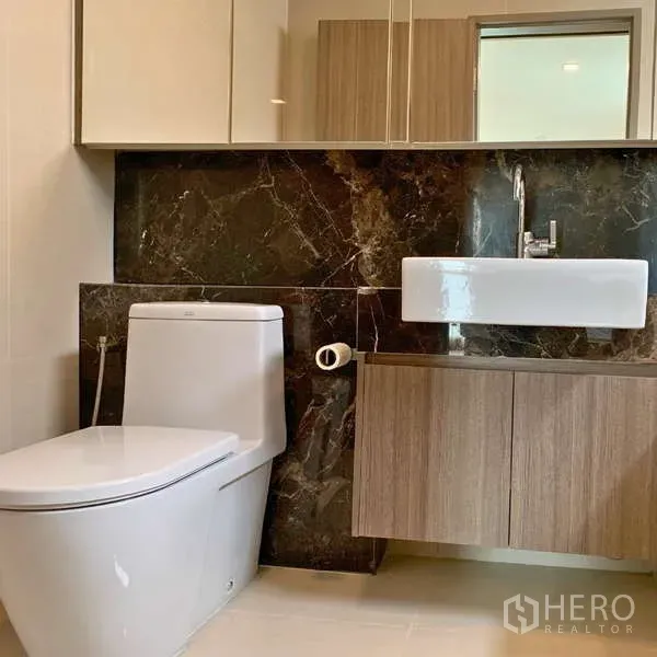 Condominium for rent - Modern bathroom with toilet, wall-mounted sink, mirrored cabinets, and dark marble backsplash.