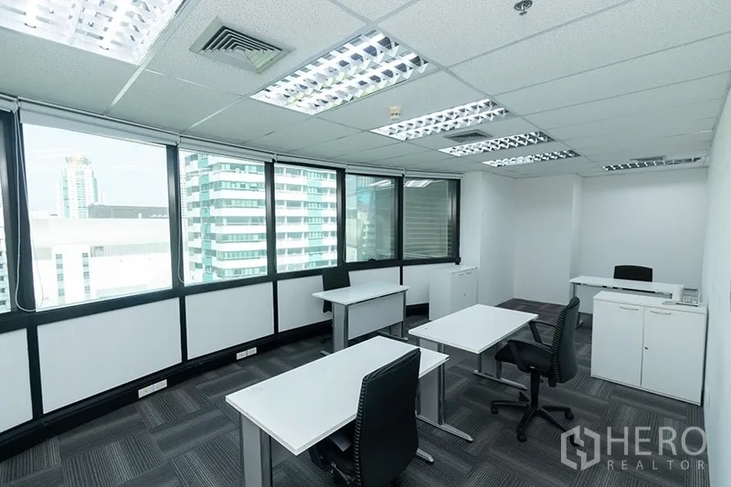 Office Space for rent - Corner office with L-shaped windows, individual desks, storage cabinets and overhead lighting.