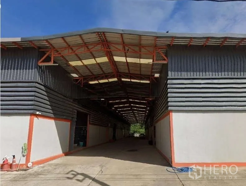 Warehouse for rent in Khlong Sam Wa, Bangkok - Exterior of twin-block steel warehouse with wide covered loading bay and concrete driveway under blue sky.