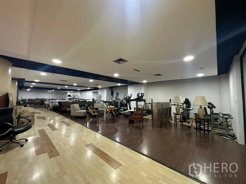 Retail Space for rent - Expansive showroom with wood flooring, lounge sets and some fitness equipment under bright recessed lighting.